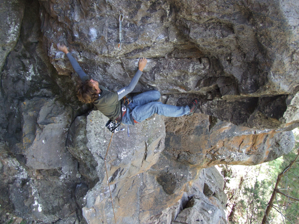 Escalador Christian Fernández del Valle colgado en posición horizontal en una vía de techo en Tamadaba, Gran Canaria. Suspendido en el aire con el cuerpo alineado con la roca, desafía la gravedad en un entorno de paredes imponentes y naturaleza salvaje.