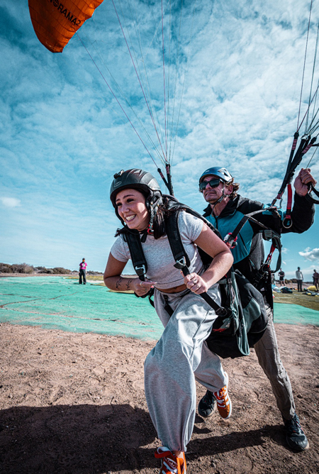 "Despegue en parapente biplaza con piloto e pasajero en primer plano, listos para volar.