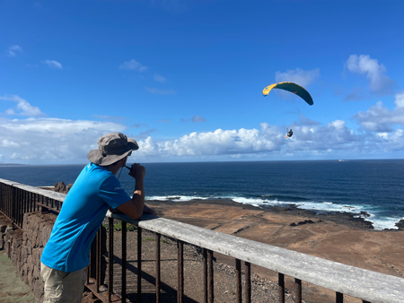 Guía de parapente dando indicaciones por radio mientras un piloto vuela sobre Las Coloradas, Gran Canaria.