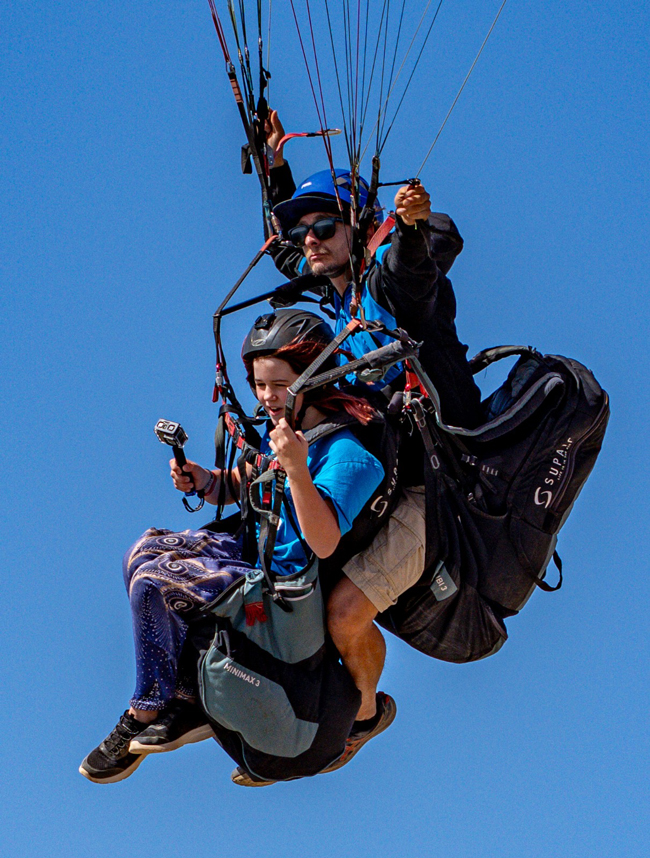 Christian Fernández Piloto de parapente realizando un vuelo en tándem con una joven pasajera, flotando en el cielo azul.